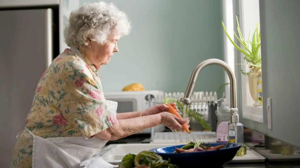 eine Seniorin schält gerade eine Möhre unterm Wasserhahn