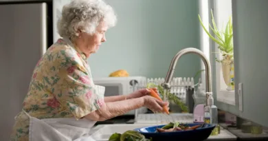 eine Seniorin schält gerade eine Möhre unterm Wasserhahn