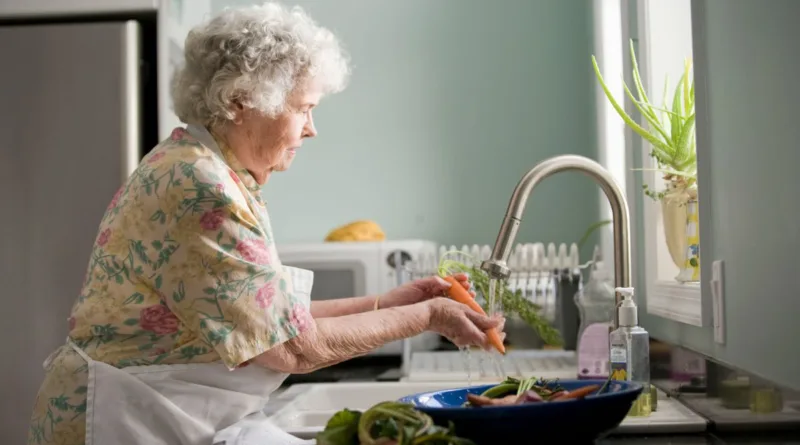 eine Seniorin schält gerade eine Möhre unterm Wasserhahn