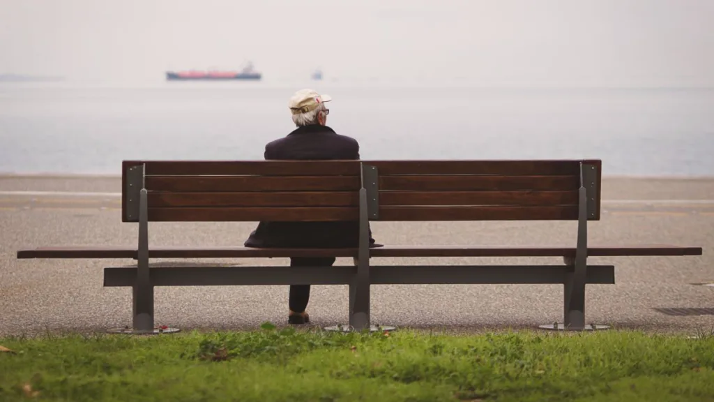 Ein Senior sitzt auf einer Bank und schaut aufs Meer