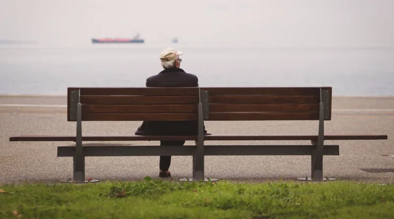 Ein Senior sitzt auf einer Bank und schaut aufs Meer