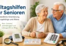 Seniorenpaar sitzt freundlich am Tisch mit Alltagshilfen wie Telefon, Lupe, Blutdruckmessgerät und Medikamentenbox