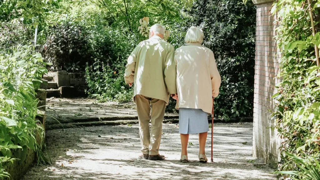 ein älteres Paar geht mit gehstöcken einen Weg entlang
