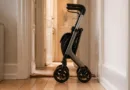 Kompakter dreirädriger Rollator in schmalem Flur, faltbar, seitliche Ansicht