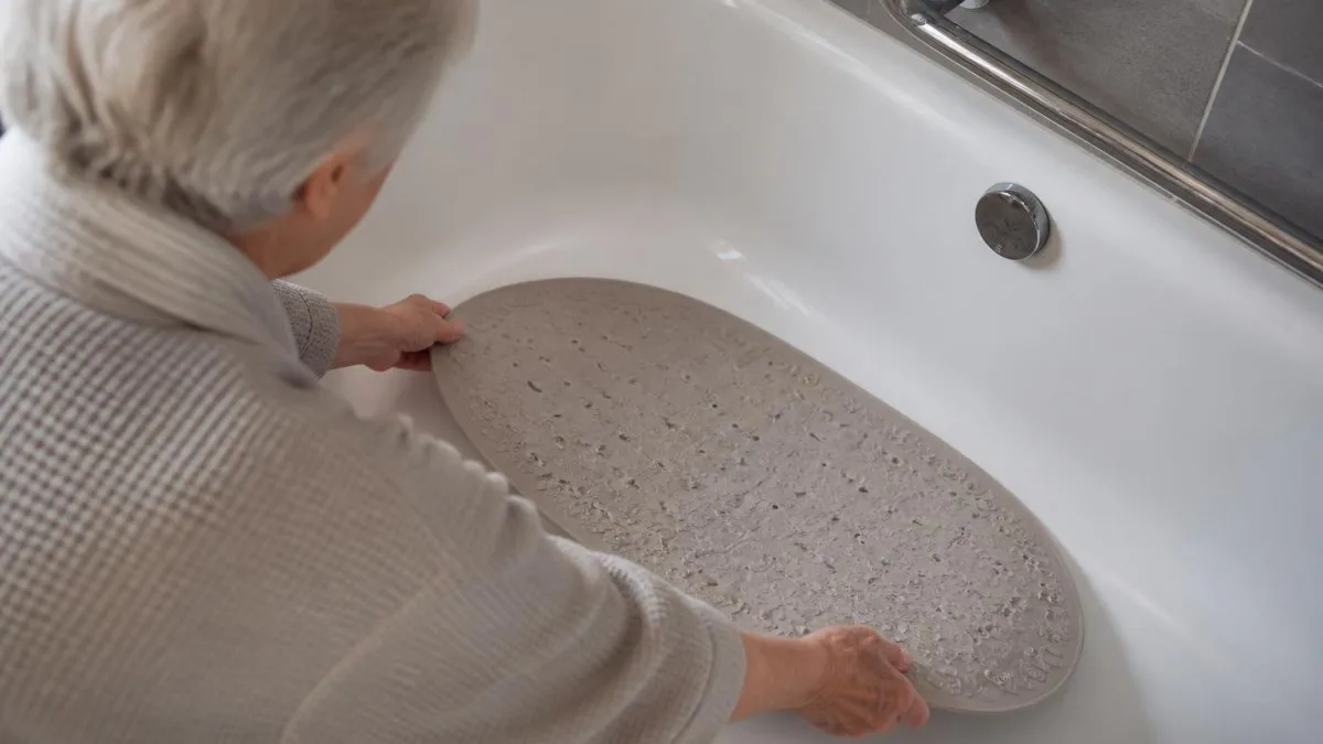 Senior positioniert eine ovale rutschfeste Badewannenmatte mit den Händen in der Wanne